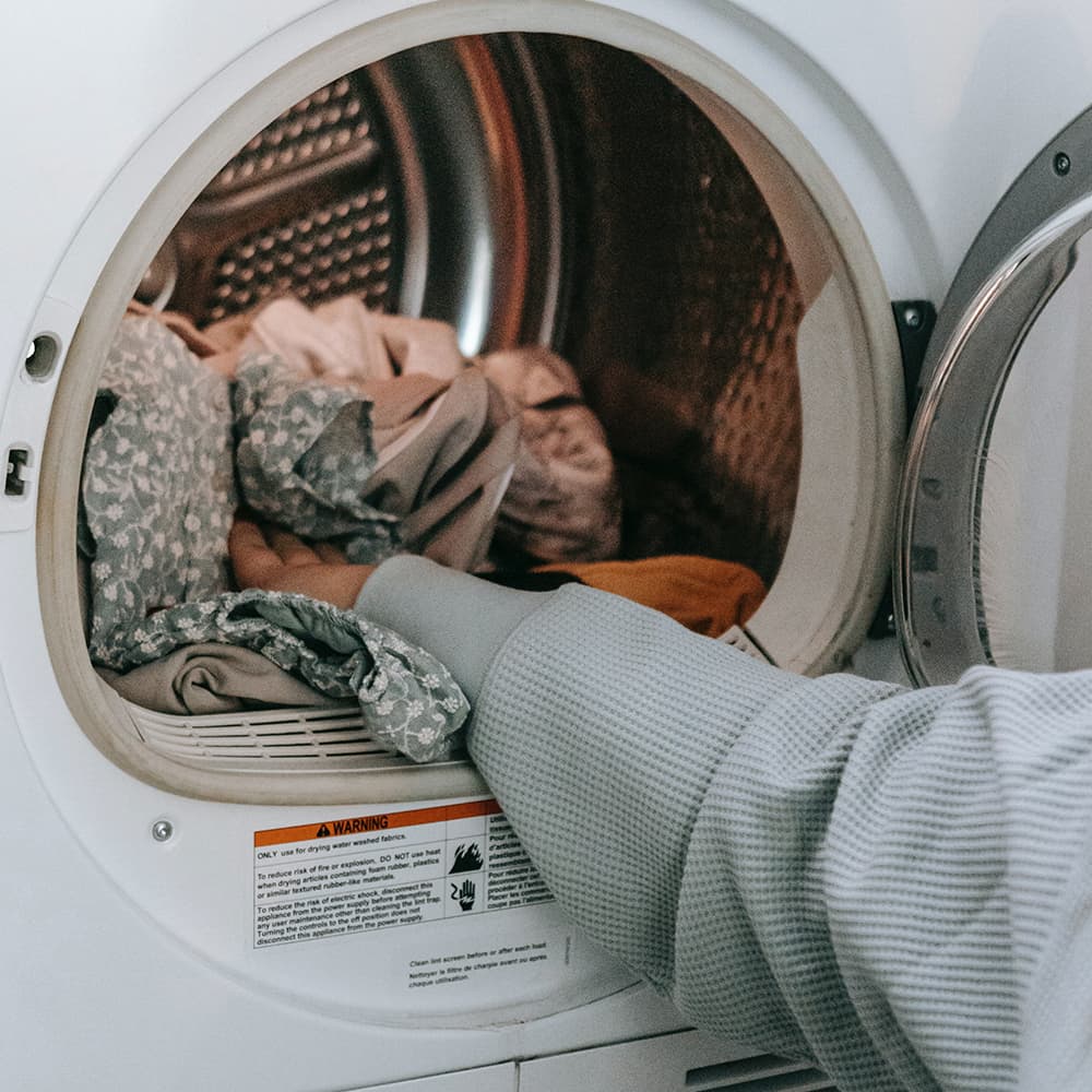 A hand adding laundry to a drying machine