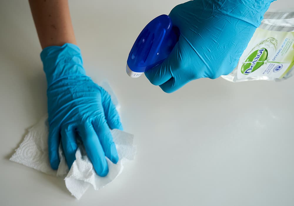 A person cleaning a surface with disinfectant spray and blue gloves