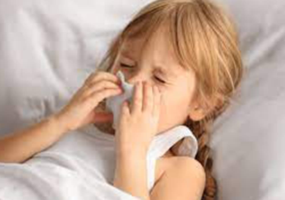 Photo of a child laying in bed and blowing her nose